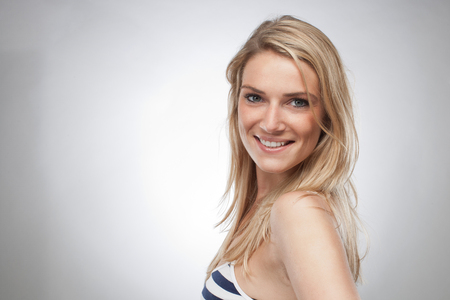 Close up Smiling Young Woman with Blond Hair in Trendy Outfit, Wearing Sleeveless Stripe Tops. Looking at the Camera. Isolated on Gray Background.の写真素材