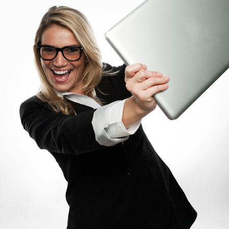 Exuberant excited young blond businesswoman in glasses laughing and cheering as she brandishes her laptop towards the cameraの写真素材