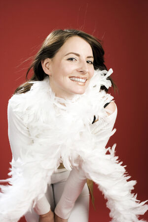 White Christmas Outfit Concept - Happy Young Woman in White Outfit with Feathery Scarf, Looking at the Camera. Isolated on Red Background.の写真素材