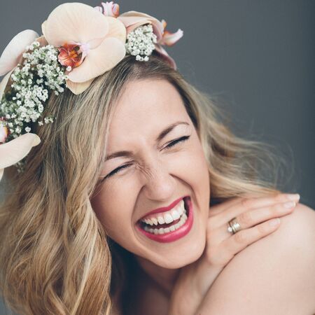 Candid portrait of a gorgeous laughing vivacious bride with long blond hair wearing a headband of pink orchids, close up head shotの写真素材