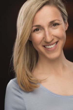 Portrait of a Cheerful Blond Young Lady Smiling at the Camera on a Dark Brown Background. Captured in Close upの写真素材