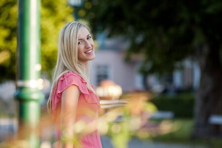 Half Body Shot of a Pretty Blond Young Woman Standing on the Road Side beside a Post and Smiling at the Camera.の写真素材