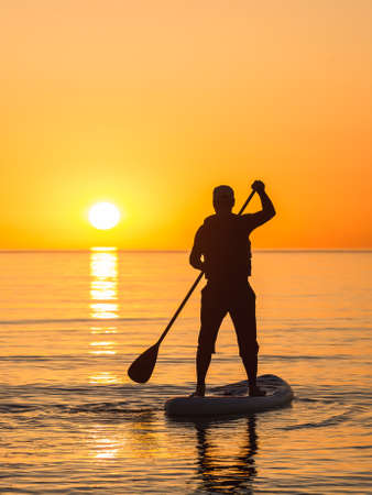 A man is rowing across the ocean on a SUP board against the background of the rising sun. Stand up paddleboarding.の写真素材