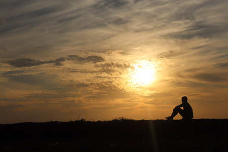 Silhouette of a man sitting on a hill at sunset.の写真素材