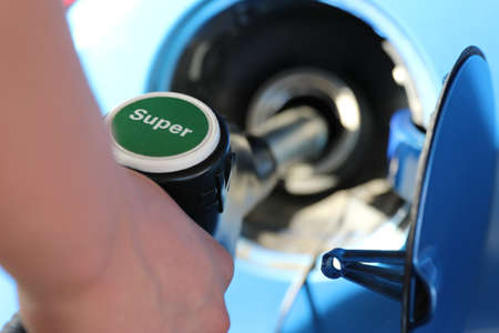 White car refueling at gas station with green fuel nozzle.