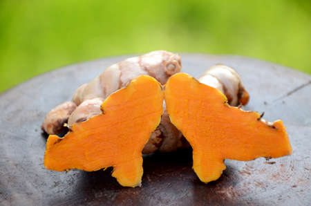 the slice brown orange ripe turmeric on the green brown wooden background.