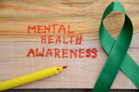 the green ribbon cross with red writing mental health awareness concept on the wooden background.の写真素材