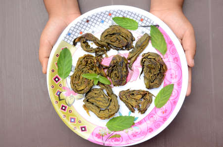 closeup the fried arabic leaves food with green mint in the plate hold hand over out of focus brown...