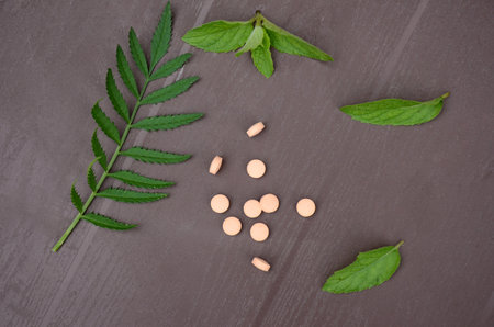 closeup bunch the pink color small medicines tablet with green mint and green leaves over out of focus on purple background.の写真素材