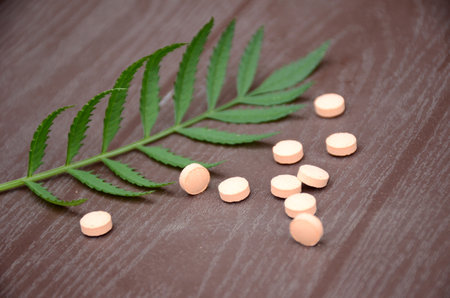 closeup bunch the pink color small medicines tablet with green leaves over out of focus on purple background.の写真素材
