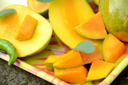 closeup the sliced ripe green yellow mango fruit with green mint leaves and chilly in the tray over...