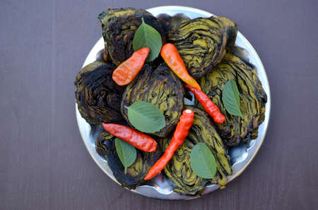 closeup the bunch green brown arabic leaves fried food with red chilly and green mint in the steel plate over out of focus grey brown background.の写真素材