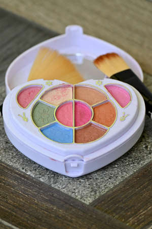 closeup the white plastic multicolor makeup kit with brown color brush over out of focus grey brown...
