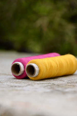 closeup the pair of pink yellow thread reels over out of focus grey green background.の写真素材