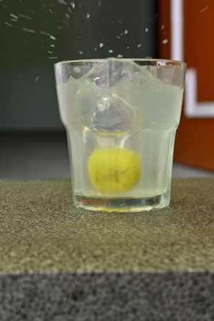 closeup the lemon juice flow in the glass over out of focus grey brown background.