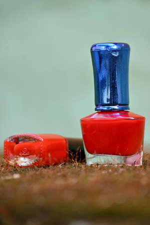 closeup the pair of red color nail paint glass bottle with blue black cap over out of focus grey...