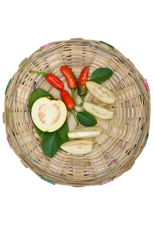 closeup the bunch ripe yellow white guava fruit sliced with red chilly and green leaf in the brown basket soft focus natural white brown background.の写真素材