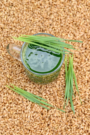 closeup the sliced green ripe wheat grass juice in the glass with wheat grass leaves and brown wheat berries soft focus natural brown background.の写真素材