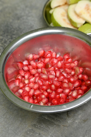 closeup the bunch red yellow ripe pomegranate seeds in the metal bowl soft focus natural red grey background.の写真素材