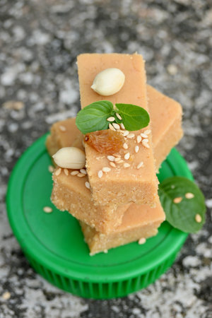 closeup the bunch brown color condensed milk sweet with green mint and pea nut,sesame grain,drilled grapes on the green plastic plate soft focus grey brown background.の写真素材