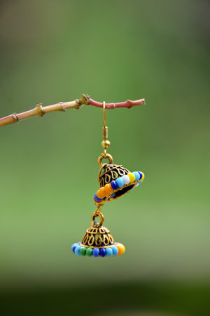 closeup the pair of golden blue color ear ring with beads hold on the plant branch soft focus...