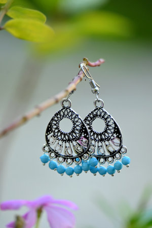 closeup the pair of silver metal ear ring with sky blue color beads hold on the plant branch soft focus natural green brown background.の写真素材