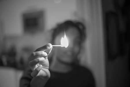 A woman holding a matchstick with fire flame in her handの写真素材