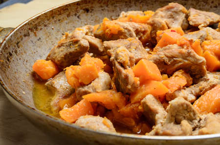 Fried pieces of meat and pumpkin in a pan on a wooden tableの写真素材