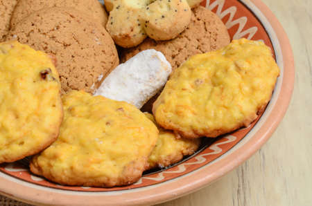 Different cookies in a clay plate on a wooden table, top view.の写真素材