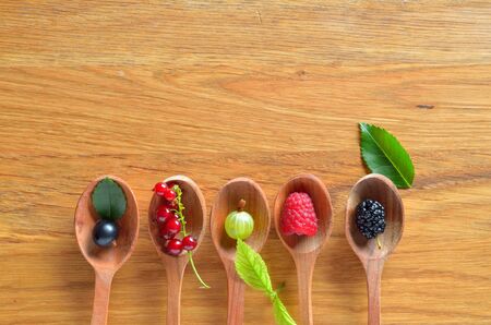 Top view of berries mixed (raspberry, black currant, red currant, gooseberry, blackberry) on wooden spoons over structured wooden board. Agriculture, Gardening, Harvest Concept. Background with space for text.の写真素材