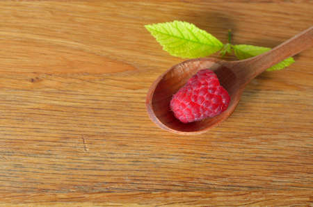 Wooden spoon with raspberry with leaves in a wooden board.の写真素材