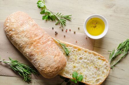 Sliced bread ciabatta watered with extra virgin olive oil with herbs  on wooden background. View...