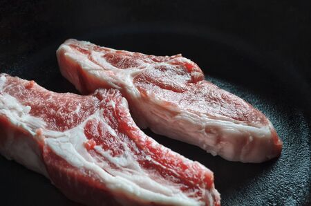 two pieces of raw, fresh meat on the bone in a cast iron frying pan, close-upの写真素材