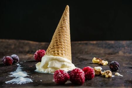 Fallen vanilla ice cream in a waffle cone on a dark, textured metal surface.の写真素材