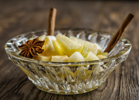 Melon dessert with sticks of cinnamon and an asterisk of an anise, in a glass ice-cream bowl, on a wooden table.の写真素材