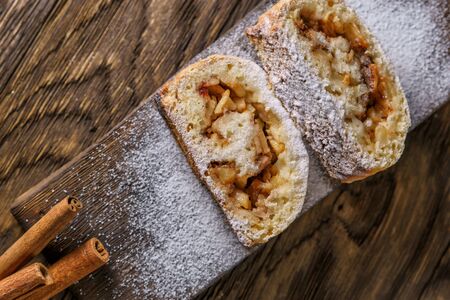 Portion dessert, strudel, with apples, nuts and cinnamon sprinkled icing sugar, laid out on an old wooden board.の写真素材