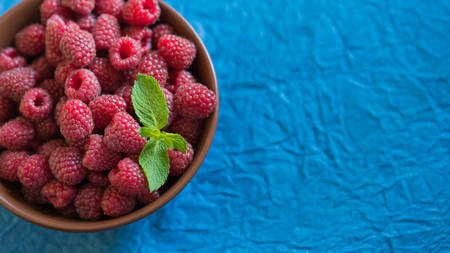 Fresh raspberry in ceramic bowl on the blue backgroundの写真素材