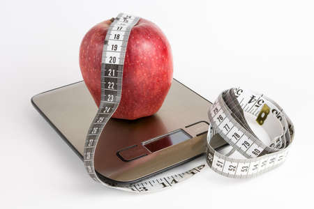 Apple on weight scale and measuring tape with white backgroundの写真素材