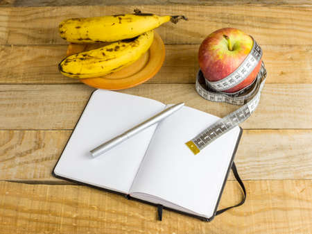 Apple with measuring tape, banana and notebook on wooden tableの写真素材