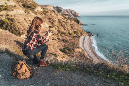 Young hip woman with a backpack exploring and photographing the coast on a beautiful day. Concept of exploration and adventuresの写真素材