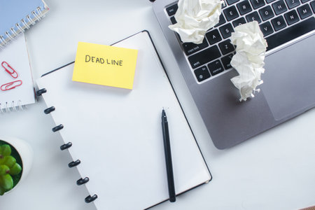 office desk top view with blank notebook and sticky note with deadline textの写真素材