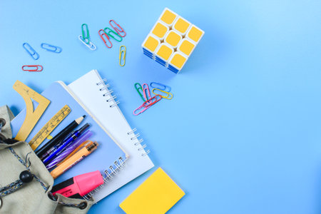 stationery in a small school bag with a rubik on blue background
