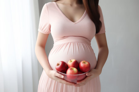 Pregnant woman holding bowl with apples on light background, closeupの素材