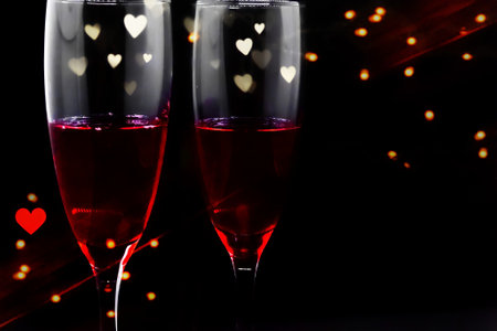 Valentine's day romantic background, two glasses of red wine close-up on bokeh background of hearts, dark black backgroundの写真素材