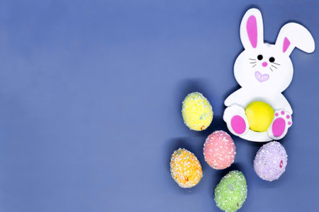 Flat lay Easter background. Toy rabbit and colorful painted eggs on a blue background.