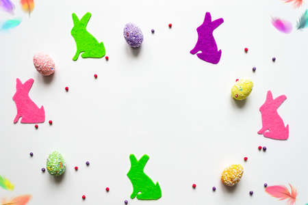 Flat lay easter background colored bunnies and eggs on white background with place for text.