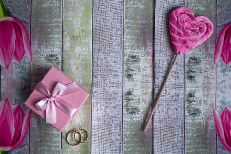 Valentine's day background with a gift in a pink box, wedding rings and a sweet lollipop in the form...