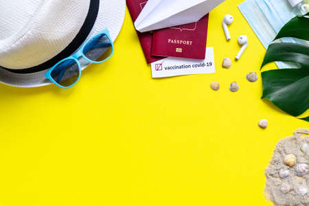 Flat lay concept of travel in new reality with coronavirus pandemic. Leisure accessories hat, sunglasses, medical mask and sanitizer, passport with Covid-19 vaccination stamp on yellow background.の写真素材