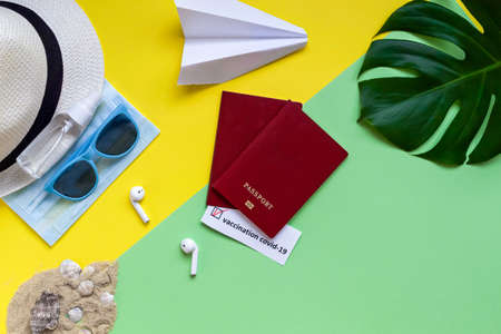 Flat lay on travel accessories with coronavirus on yellow and green background. Passport with a stamp of vaccination against the virus. Covid-19 and travel concept.の写真素材