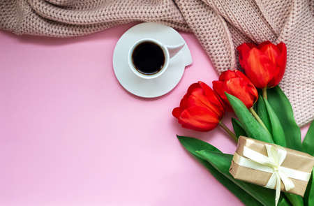 Flat greeting card composition for mothers day, international womens day. Light pink background with place for text. Red tulips, cup of black coffee, knitted pink scarf and holiday gift.の写真素材